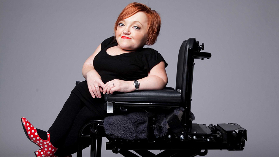 image of stella young, a white woman with red hair sitting in a black wheelchair, wearing red and white polka dot shoes